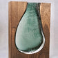 a green vase sitting on top of a wooden shelf 